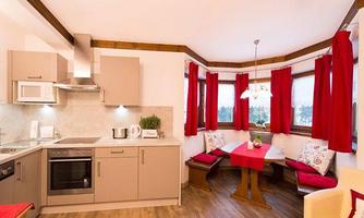 A modern kitchen with wooden furniture and red curtains. A dining table with benches invites you to linger.