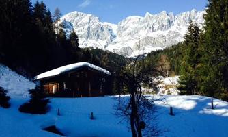 A cozy cabin in the snow with majestic mountains in the background. The landscape is wintry and idyllic.