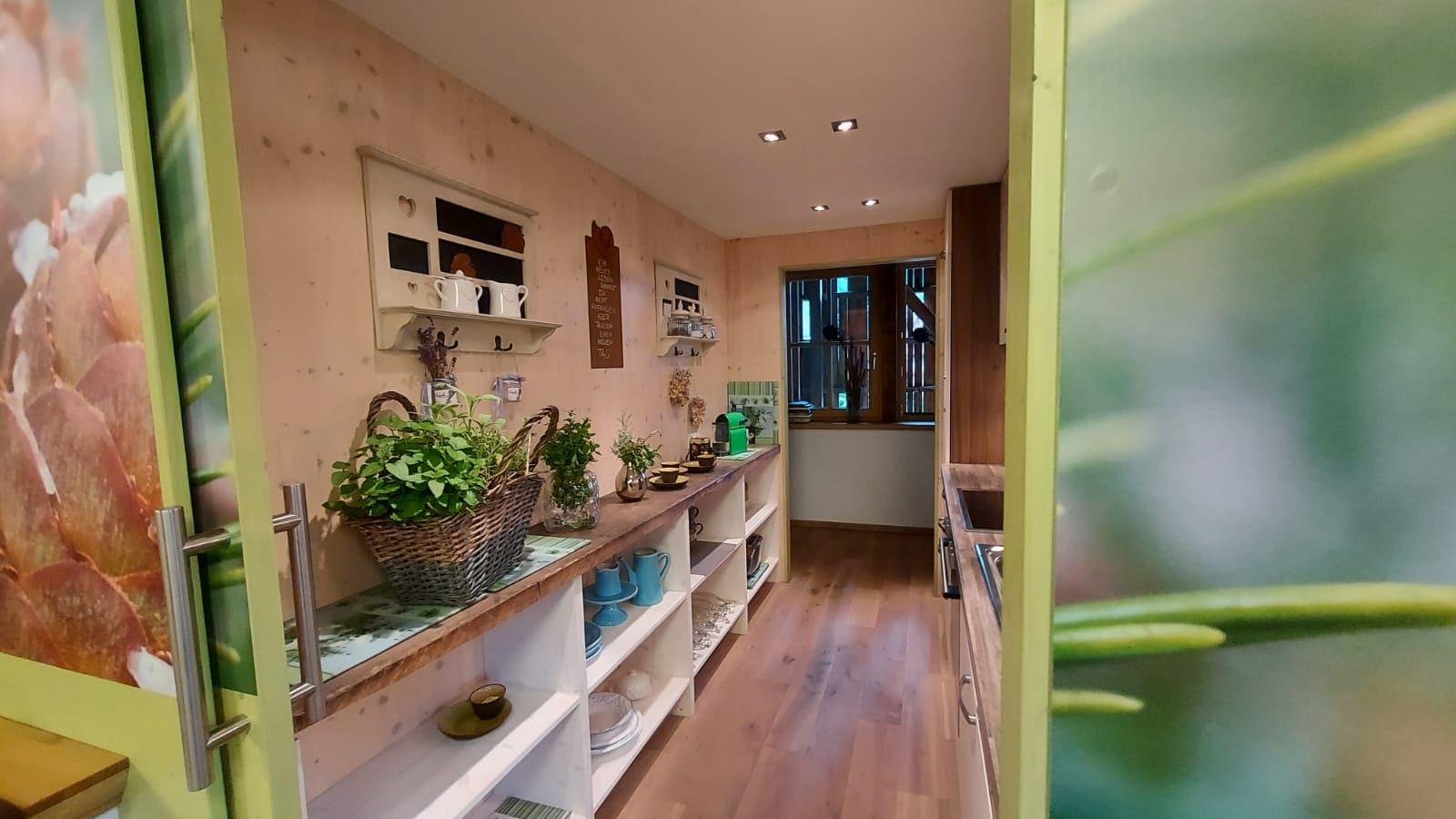 A cozy kitchen with wooden furniture and plants on the countertop. The room has plenty of daylight and an inviting atmosphere.