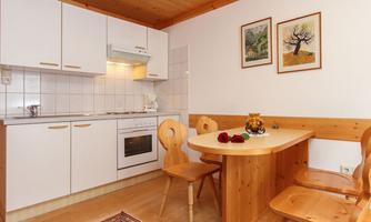 A cozy kitchen with white cabinets and a wooden ceiling. A round table with several chairs and decoration is also visible.