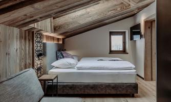 A cozy bedroom with wooden beams and a large bed. The decor is modern and stylish, with a small seating area and a window.