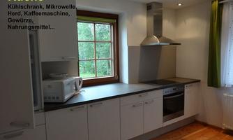 A modern kitchen with white cabinets and a window front. Equipped with a stove, microwave, and coffee maker.