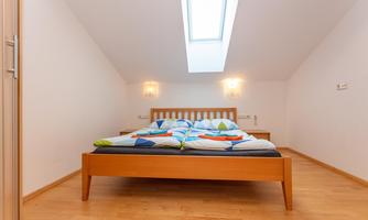 A modern bedroom with a wooden bed and colorful blankets. Large skylights provide plenty of daylight.