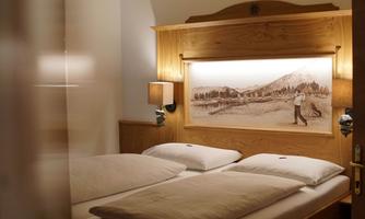 A cozy bedroom with a wooden frame bed and two pillows. A beautiful picture of a landscape hangs on the wall.
