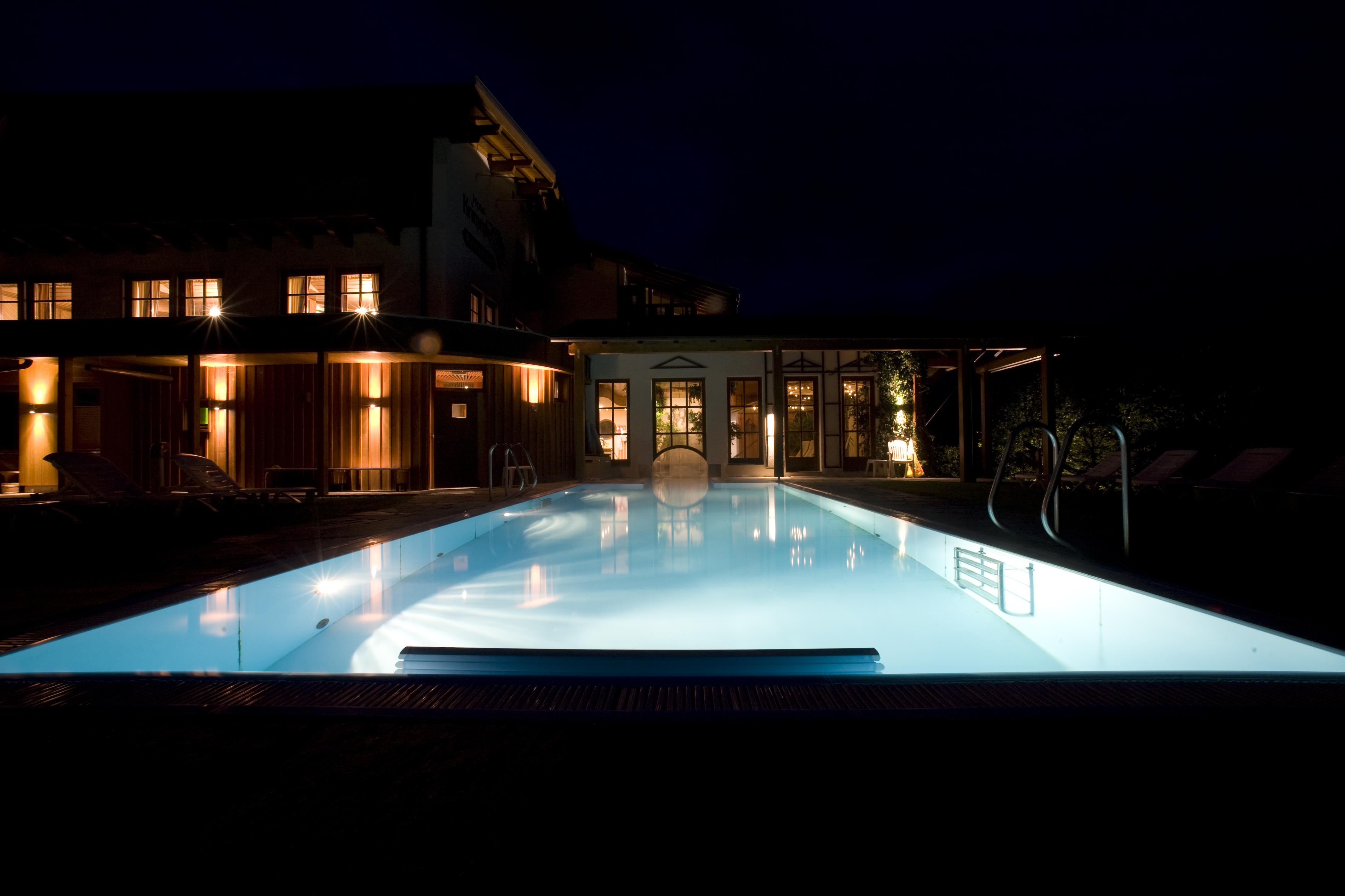 A lit pool at night, surrounded by a stylish building. Soft light reflects on the water's surface.