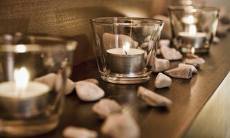 Several tealights in glass containers are placed on a wooden surface, surrounded by small stones. The warm light creates a cozy atmosphere.