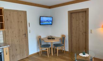 A cozy room with wooden paneling and a small table with chairs. A television hangs on the wall, and the floor is made of wood.