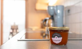 A jar of jam is sitting on a kitchen counter. Kitchen appliances are visible in the background.
