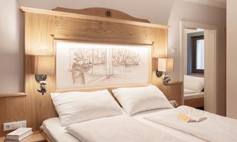 A cozy bedroom with a double bed and wooden details. An artistic picture depicting a landscape hangs on the wall.