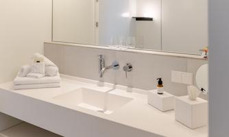 A modern bathroom with a simple washbasin and a large mirror. There are fresh towels and some toiletries on the shelf.