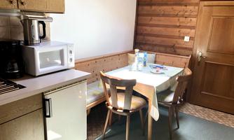 A cozy kitchen with wooden walls and a table with chairs. On the countertop, there is a coffee maker and a microwave.