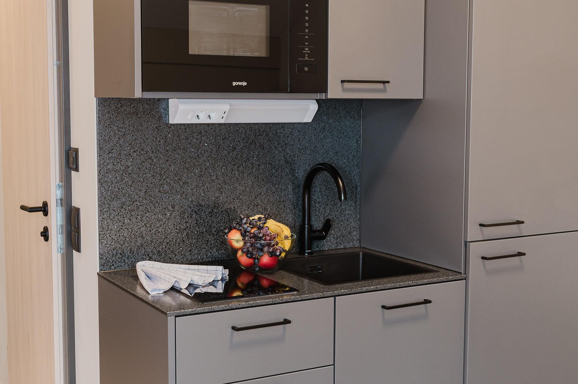 A modern kitchen with gray cabinets and a granite countertop. On the sink, there is a bowl of fresh fruit.