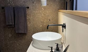 A modern bathroom with a round sink and elegant fittings. In the background, two towels hang and a stylish pendant light provides illumination.