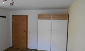 A simple room with a white cabinet and a wooden door. The floor is made of wood and the walls are light.