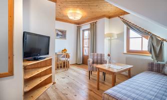 A cozy living room with wooden floor and a bright, inviting atmosphere. The furnishings consist of a sofa, a table, and a television.