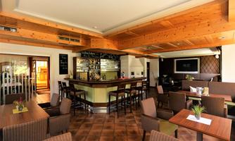 A cozy restaurant interior with a wooden ceiling and a central bar counter. The tables are neatly set and create an inviting atmosphere.