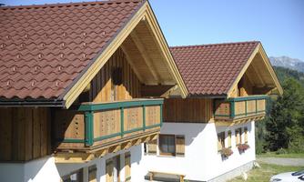 Two beautiful chalets with wooden cladding and red-coated roofs. The buildings are surrounded by a green landscape.
