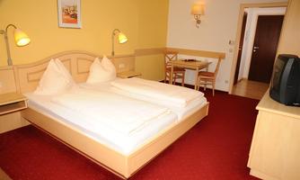 A cozy hotel room with a double bed and two pillows. There is a small table and chairs as well as a television corner.