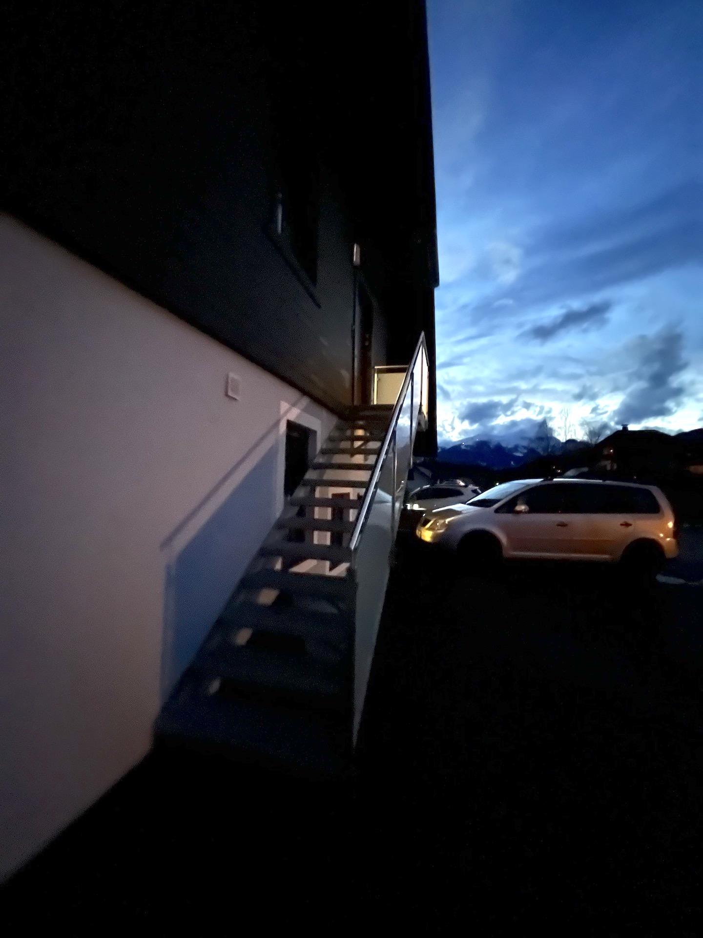 A staircase on the outside of a building leads upwards. In the background, the evening sky with clouds is visible.