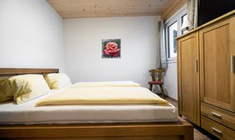 A simple bedroom with two beds and yellow bedcovers. On the wall hangs a picture of a red flower.