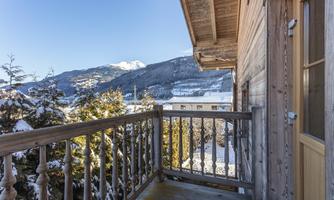 A balcony with a wooden railing overlooking snow-covered mountains. The sky is blue and the surroundings are quiet and picturesque.