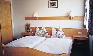 A cozy bedroom with a double bed and two decorative pillows. The walls are light, and there is a small dresser as well as a picture above the bed.