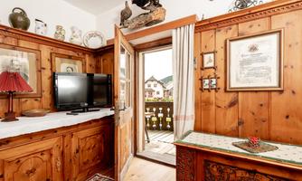 A cozy room with wooden-paneled walls. Through the open door, there is a view of the exterior and a balcony.