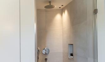 A modern shower with bright tiles and a rain showerhead. The lighting creates a pleasant atmosphere.