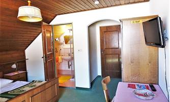 A cozy room with wooden paneling and simple furnishings. There is a bathroom, a table, and a television.
