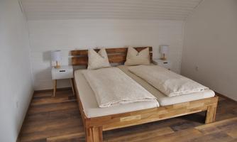 A cozy bedroom with a wooden bed and stylish bedside lamps. The room has a clean, modern look with warm wooden flooring.