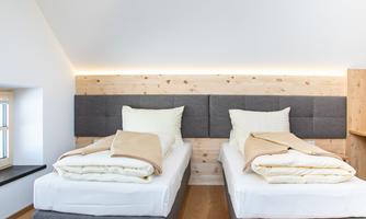 A modern bedroom with two single beds. The walls are light and the decor is simple and elegant.