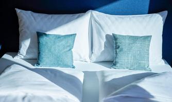 A cozy bed with white pillows and two decorative pillows in different shades of blue. The room has a calm and inviting atmosphere.