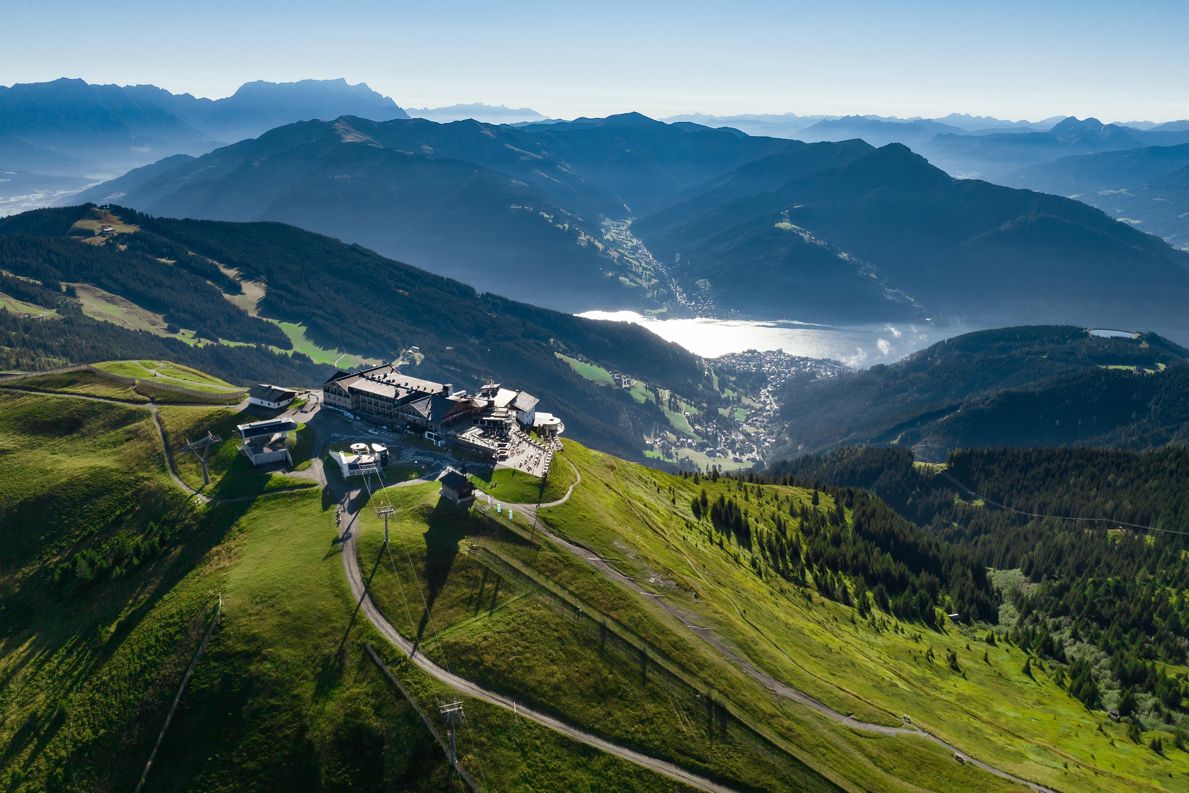 A stunning mountain landscape with green meadows and a clear sky. In the background, mountains and a calm lake can be seen.