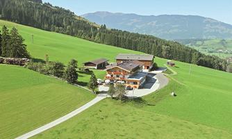 An idyllic landscape with a large farmhouse surrounded by green meadows and wooded hills. The sky is clear and nature radiates tranquility.