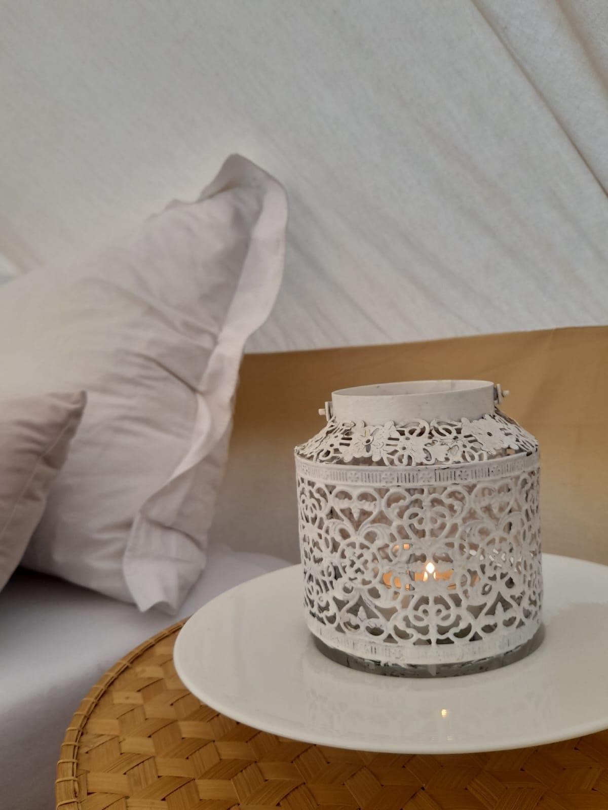 A stylish lantern made of white metal stands on a plate. In the background, soft cushions are visible, creating a cozy atmosphere.