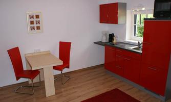 A modern kitchen with red cabinets and a small dining table. There are two red chairs and a rug in the middle of the room.