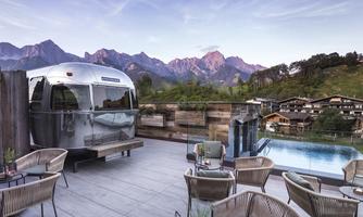A modern terrace with a silver caravan and a view of the mountains. A pool and comfortable seating invite relaxation.