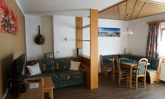 A cozy living room setup with a sofa, table, and chairs. The walls are painted in warm colors and there are decorative elements.