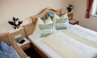 A cozy bedroom with a large double bed and a children's bed. On the bed are cushions with checkered covers.