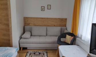 A cozy living room with a gray sofa and a chair. The walls are light and adorned with decorative pictures.