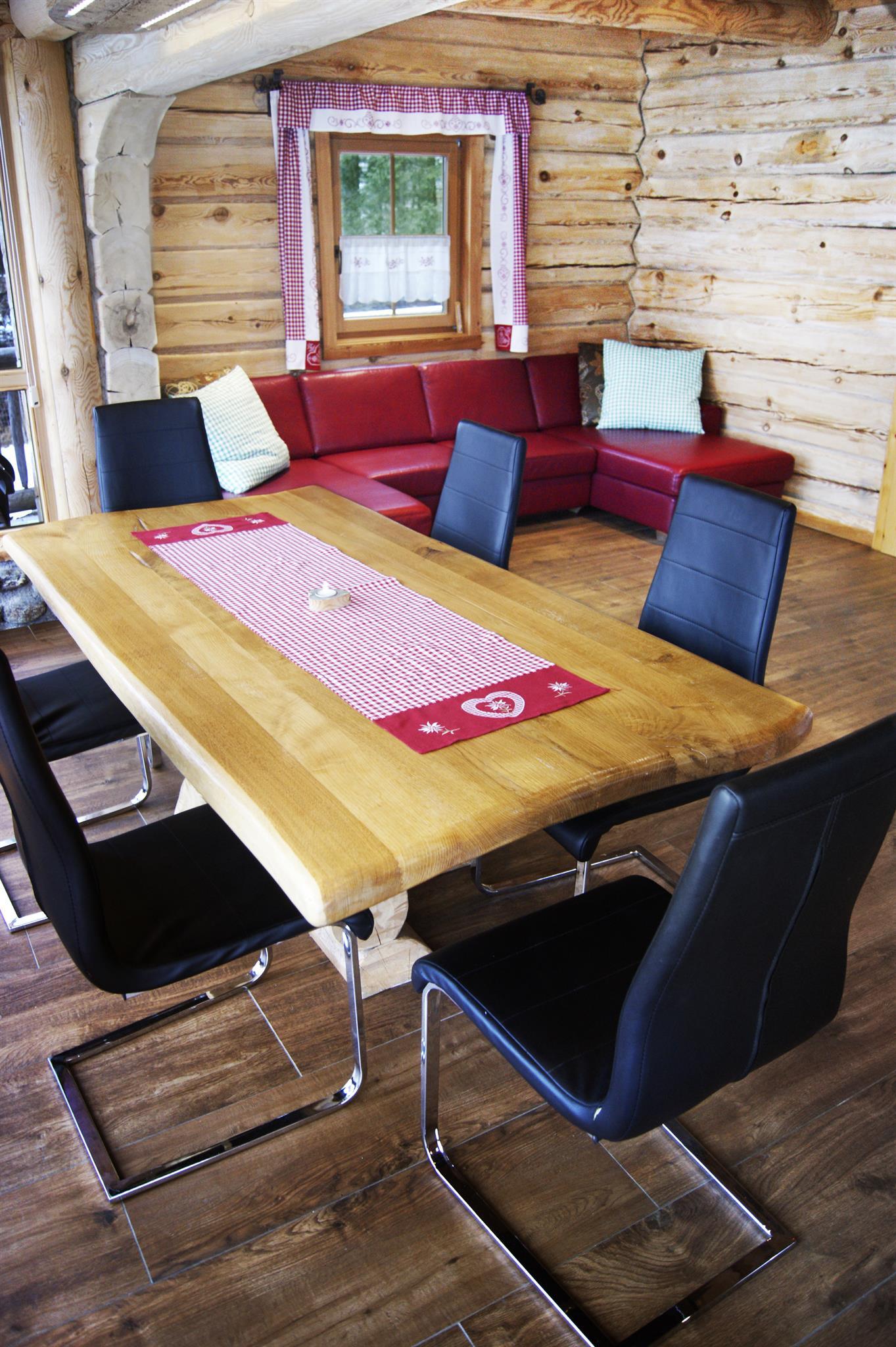 A cozy dining area in a rustic cabin. There is a wooden table with six chairs and a red couch in the background.