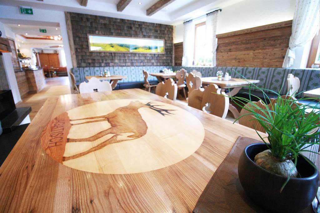 A cozy restaurant with wooden furniture and an artistically carved table. The table features an image of a deer and is surrounded by plants.