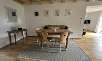 An inviting dining area with a wooden table and four chairs. The walls are decorated with modern pictures, and the floor is made of light wood.