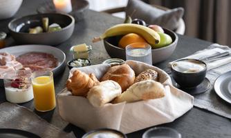 An elegant breakfast table with various foods. Fresh rolls, fruit, yogurt, and drinks are arranged.