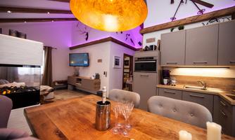 Modern kitchen with a large wooden table and elegant lighting. The space is cozily furnished with a television and a decorative atmosphere.