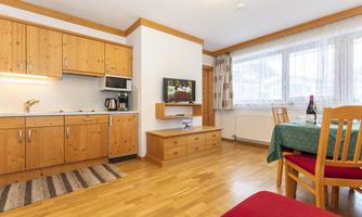 A cozy kitchen with wooden cabinets and modern appliances. In the background, there is a dining area with a table and chairs.