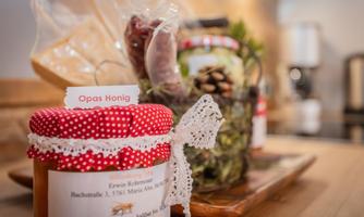 A jar of honey with a red lid and a label is visible in the foreground. Decorated jars and a rustic wooden surface are in the background.