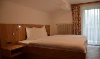 A modern bedroom with a wooden double bed and pleasant lighting. Large windows provide plenty of daylight and a view outside.