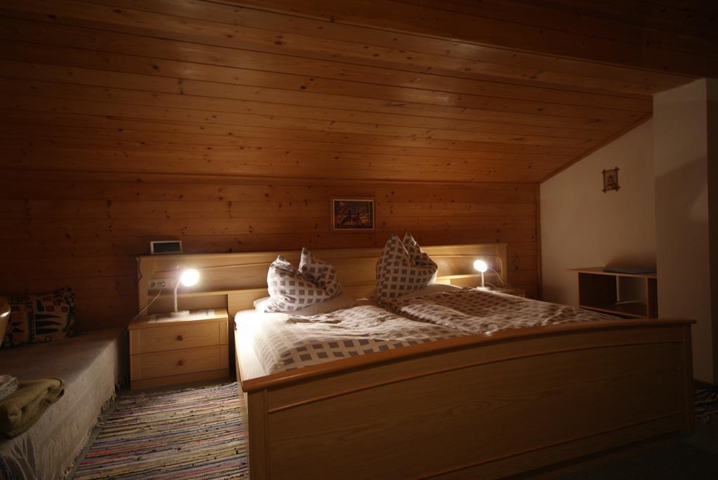 A cozy bedroom with a wooden ceiling and dimmable lighting. The bed is equipped with two pillows and blankets, and there are bedside tables next to it.