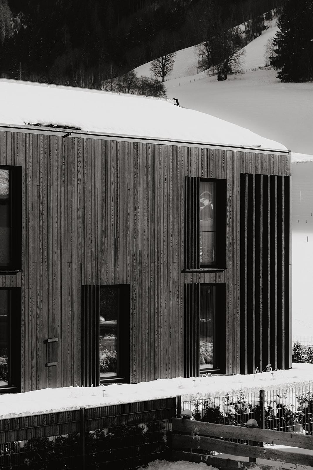 A modern wooden house in the snow with large windows. The architecture is simple and elegant, surrounded by a winter landscape.